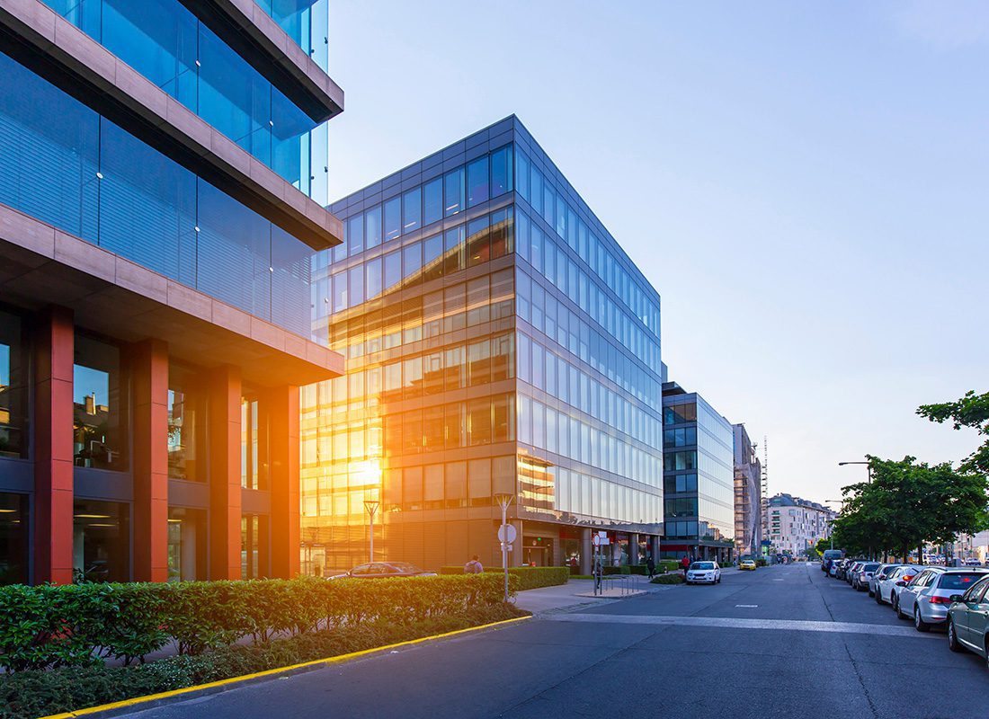 Business Insurance - Row of Modern Commercial Office Building Next to a Street with Parked Cars at Sunset with the Sunlight Reflecting Off the Glass Panels