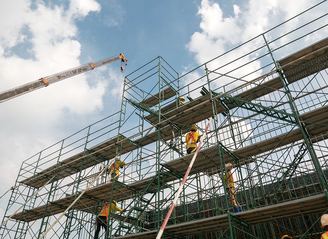 Insurance Solutions - View of Construction Workers Building Metal Scaffolding on a New Building Construction Project Against a Cloudy Blue Sky