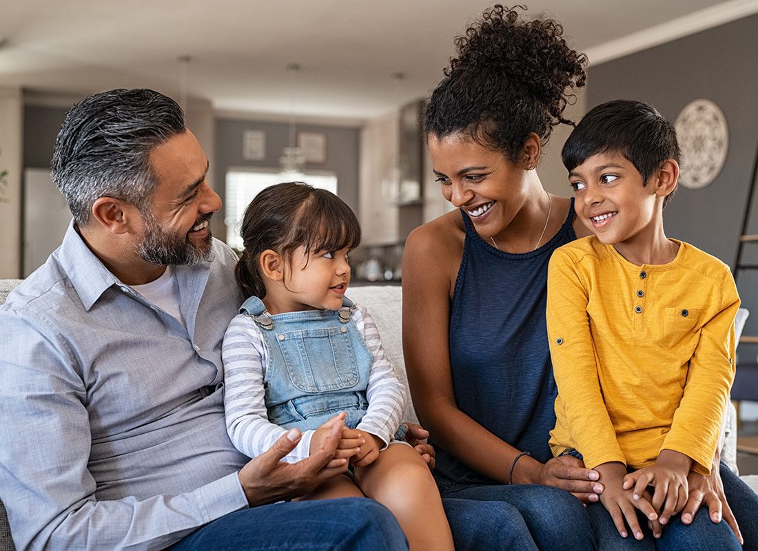 Personal Insurance - Portrait of a Cheerful Family with Two Young Kids Having Fun Spending Time Together While Sitting on a Sofa in the Living Room